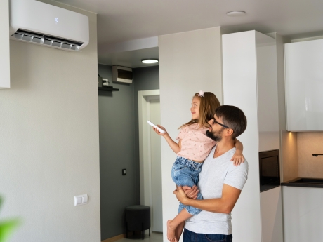 man holding his daughter who is using an air conditioning remote