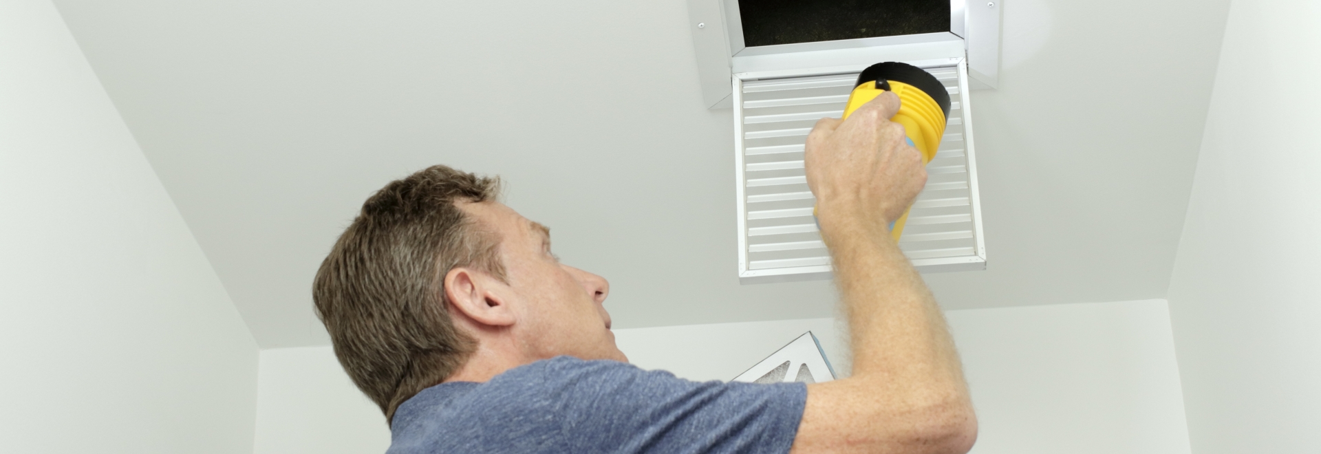 Technician Shining a Light Up a Duct Vent In the Ceiling