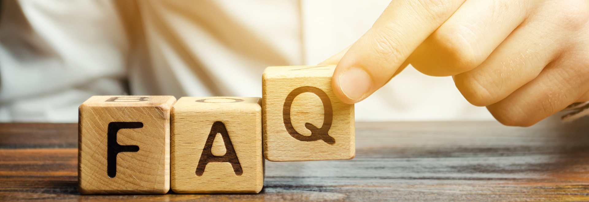 Hand Placing Wooden Blocks With Letters On Them That Spell "FAQ"