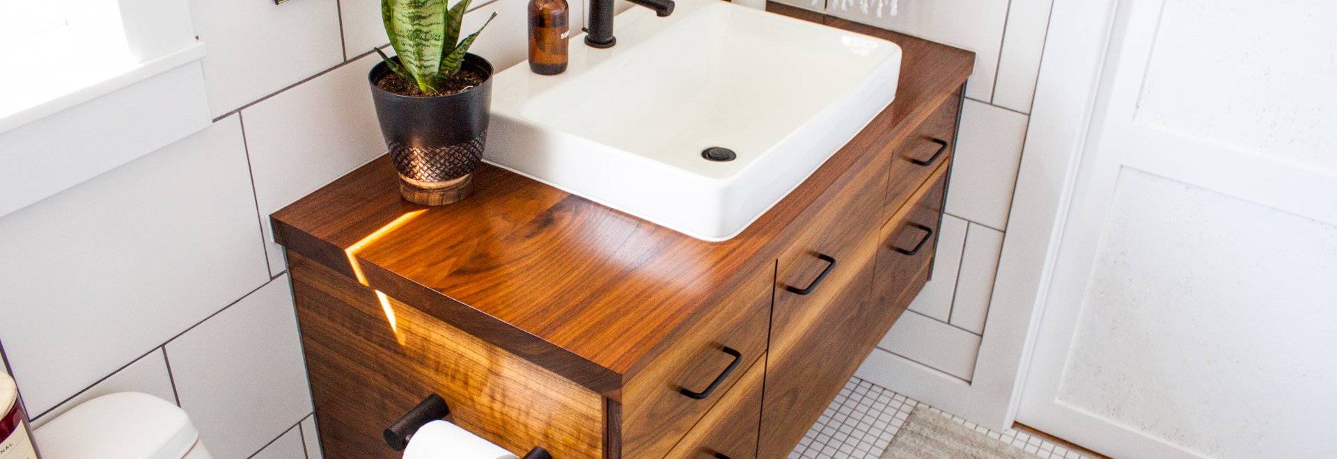 dark wooden bathroom vanity with white sink atop and snake plant to the left