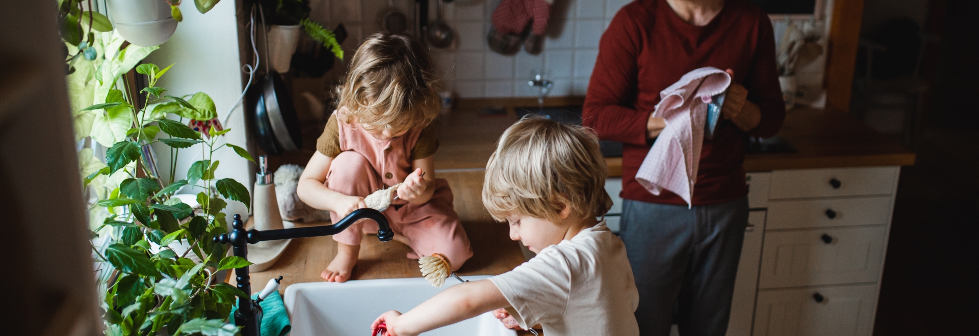 Two young kids washing dishes with their father in kitchen