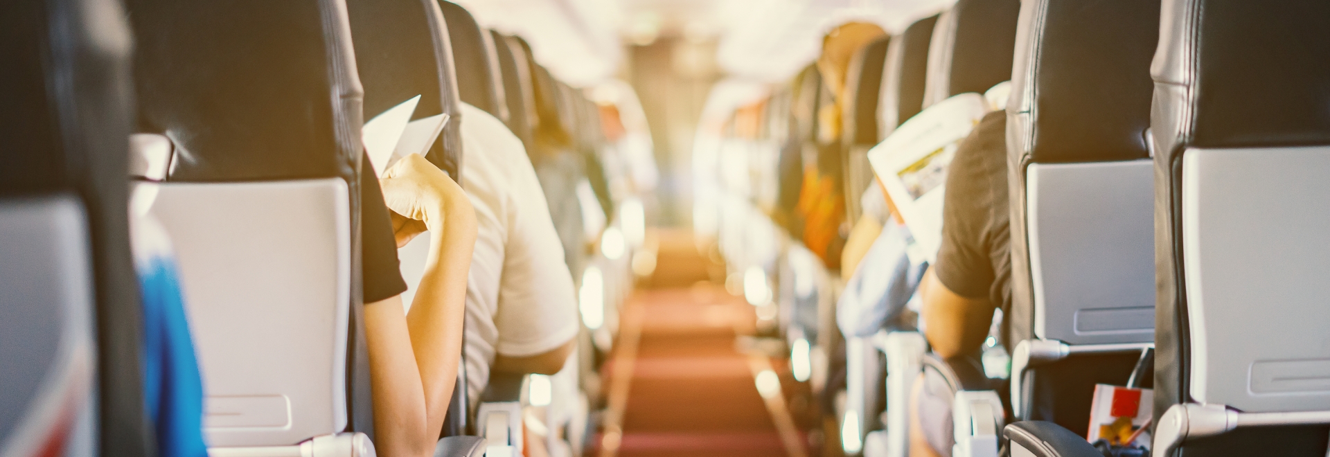 Interior of airplane with passengers sitting on seats and stewardess walking the aisle in background