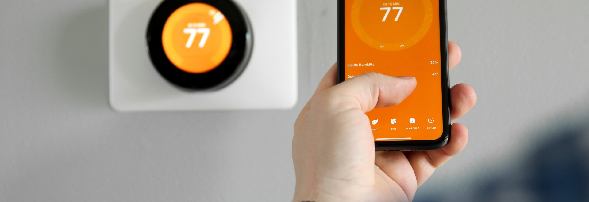 man uses his phone to control a smart thermostat