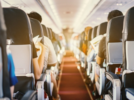 Interior of airplane with passengers sitting on seats and stewardess walking the aisle in background