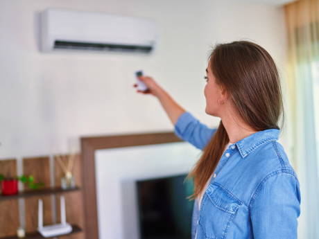 woman adjusting temperature of heat pump with a remote control at home