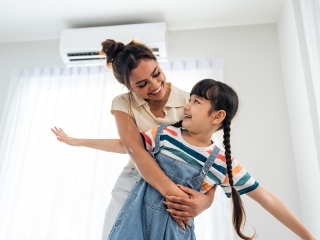 mother and daughter huge under a heat pump wall unit