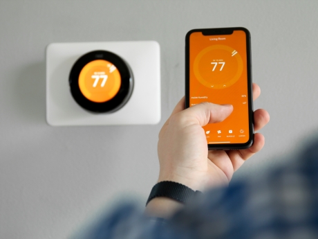 man uses his phone to control a smart thermostat