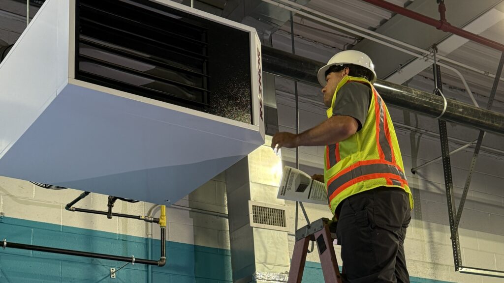 A tech fixes an HVAC system from a ladder. Princeton Air can help you decide whether to repair vs replace a commercial HVAC system.