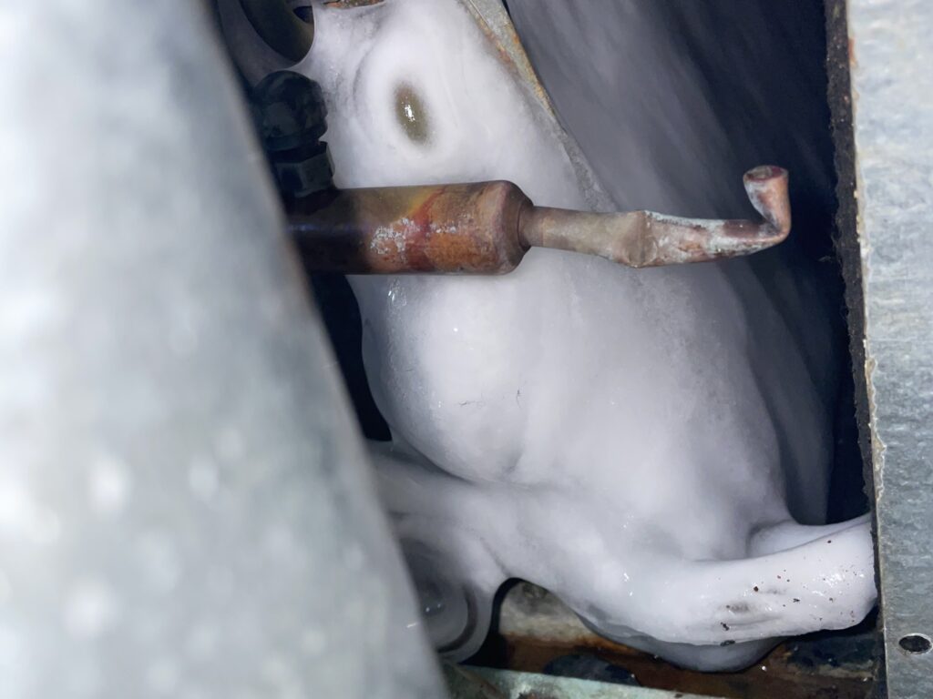 Thick ice buildup covering the evaporator coil inside a frozen ac unit in a New Jersey home